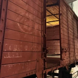 Exterior of a preserved World War II-era Belgian freight railcar with its sliding door open, showing the bare wooden interior used in Holocaust deportation transports.