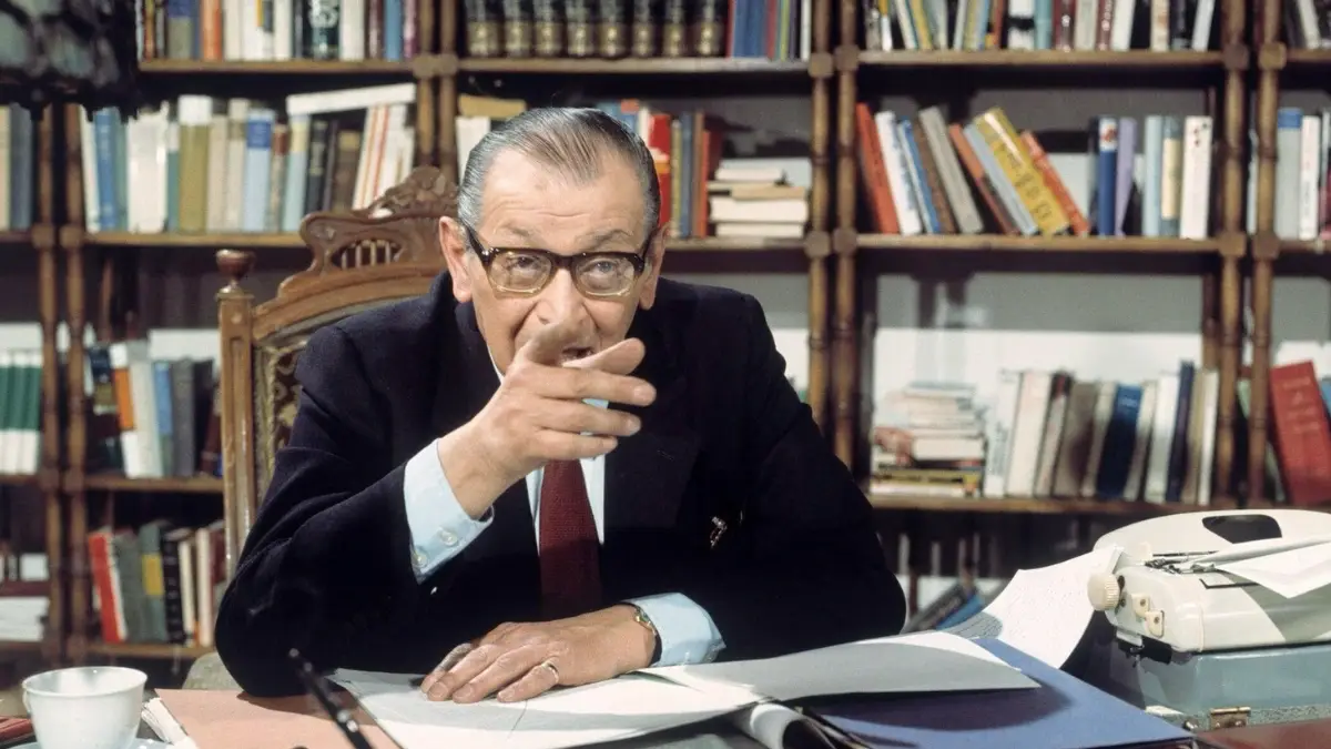 Austrian Jewish author Friedrich Torberg seated at his writing desk surrounded by bookshelves, photographed in 1970.