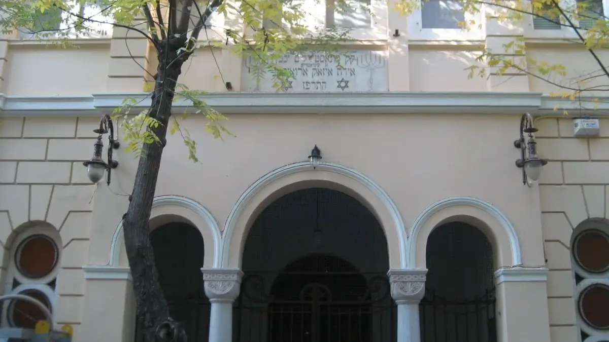 Exterior facade of the Monastir Synagogue in Thessaloniki, Greece, featuring triple arched entryways, Hebrew and Ladino inscriptions, Star of David motifs, and period wall-mounted lanterns, one of the historic sites documented in the Josephus Greek Jewish digital archive.